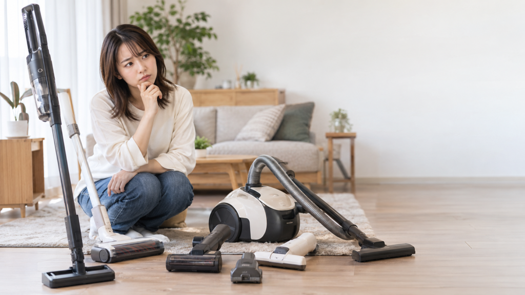 スティック掃除機、キャニスター式、床用ヘッドや小型ノズルを木床に並べて比較する女性
